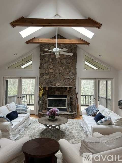 A living room with a stone fireplace and a ceiling fan.