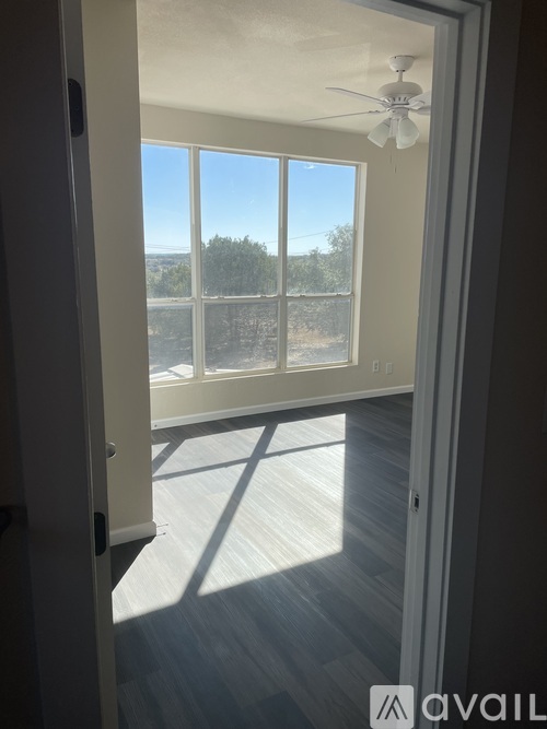 A room with a ceiling fan and a view of the outdoors through a large window.
