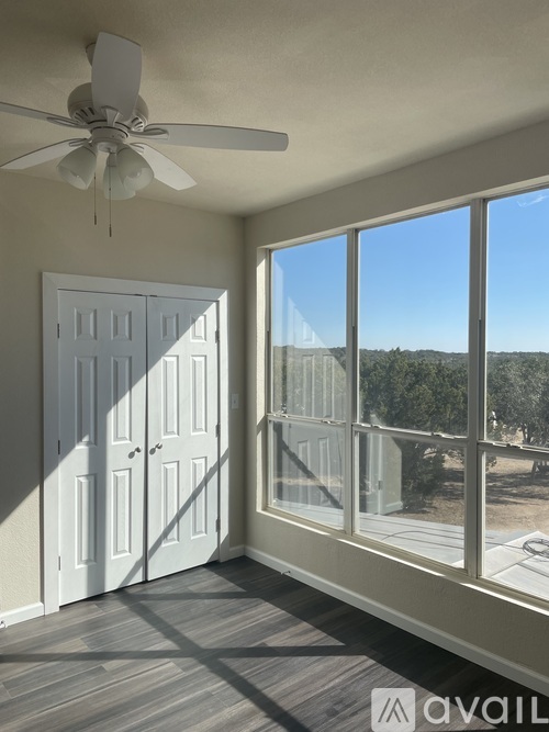 A room with a ceiling fan and a view of trees outside through the window.