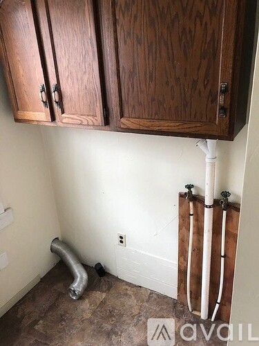 A kitchen with wooden cabinets and a white pipe running along the wall.