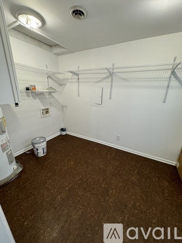 A room with white walls and brown carpeting with a white fridge on the left.