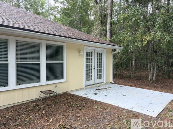 A house with a white door and windows is surrounded by trees.