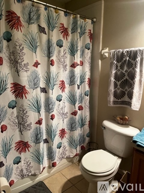 A bathroom with a white toilet and a shower curtain with a leaf pattern.