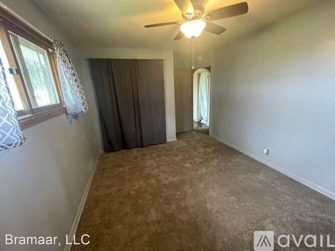 A room with a ceiling fan and a window with curtains.