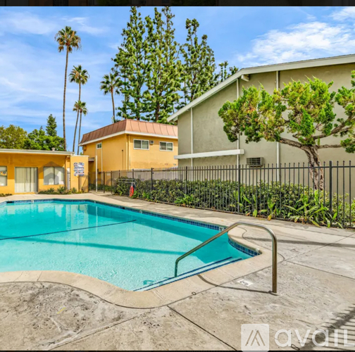 A pool surrounded by a fence and trees with a house in the background.