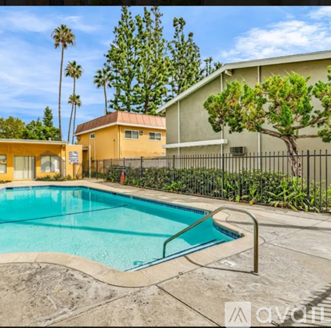 A pool surrounded by a fence and trees with a house in the background.