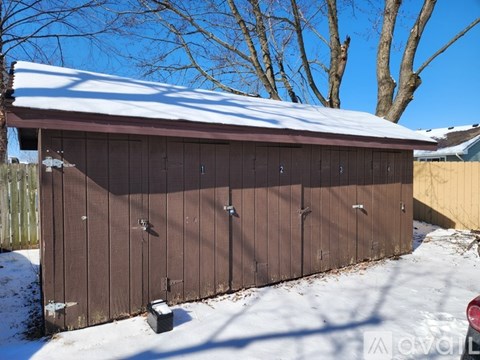 A brown wooden shed with a snow-covered roof.