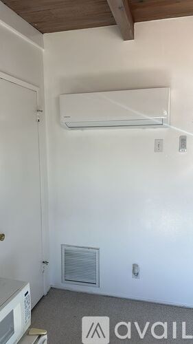 A room with a white wall and a window with a white air conditioner.