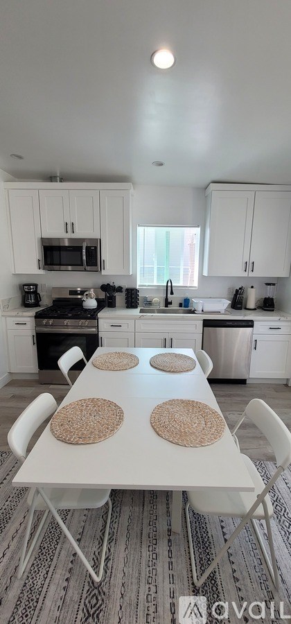 A white dining table with four chairs and four round placemats in a kitchen.