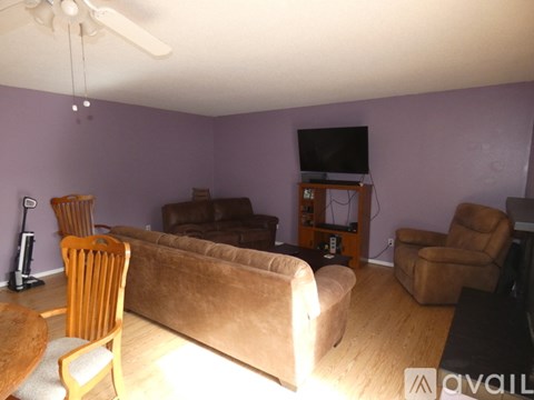 A living room with a brown couch, a wooden chair, and a television on a stand.