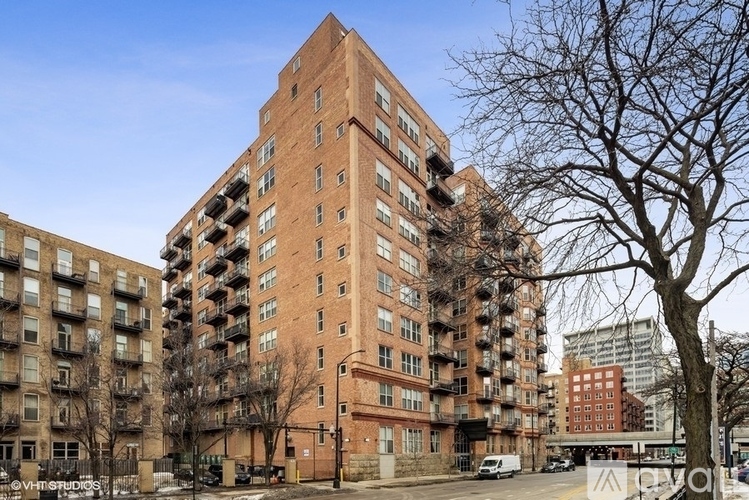 A tall red brick apartment building with a parking lot in front.