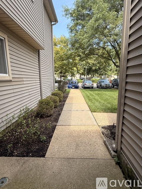 A sidewalk leads from a house to a grassy area with cars parked in the distance.