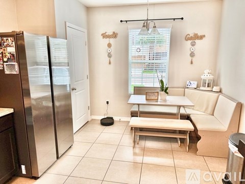 A kitchen with a refrigerator, a table with a vase of flowers, and a window with blinds.