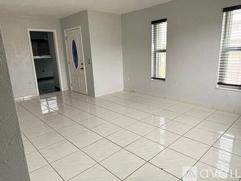 A spacious room with white tiled flooring and a door with a circular window.