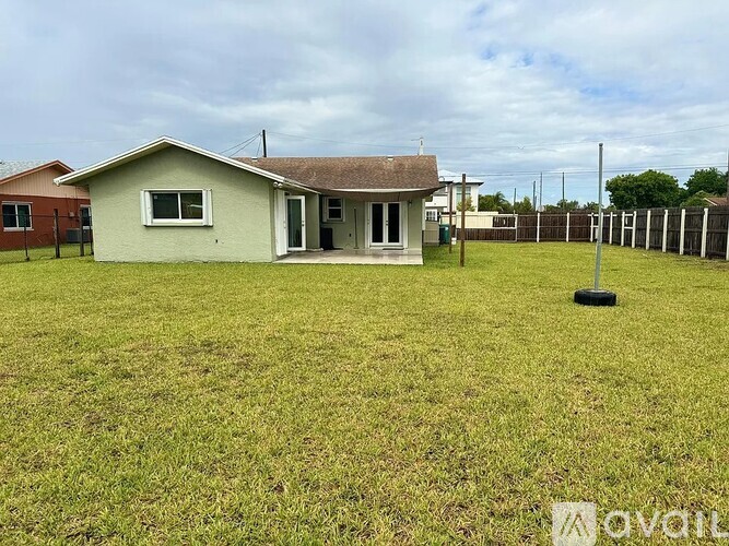 A small house with a grey roof and a white door is surrounded by a grassy field.