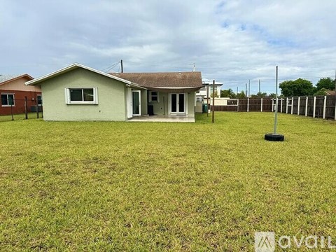 A small house with a grey roof and a white door is surrounded by a grassy field.