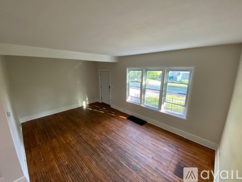 A room with wooden flooring and a window overlooking a green area.