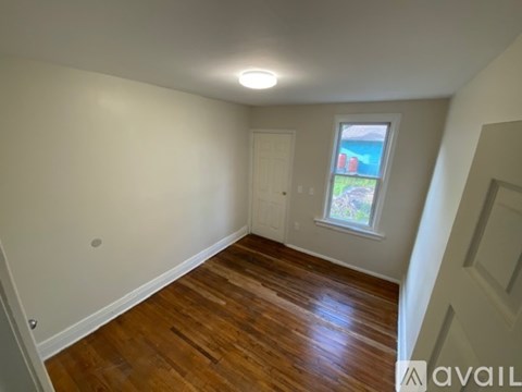A room with wooden floors and a window showing a view of a pool and trees.