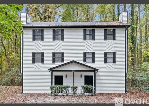 A white house with black shutters is surrounded by trees.