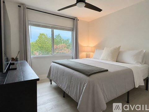 A bedroom with a bed, a fan, and a window with curtains.