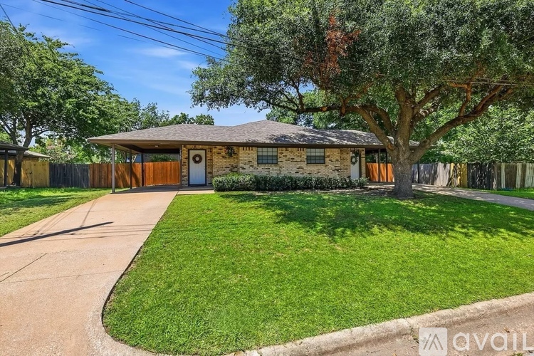 A house with a brown roof and a brown fence is surrounded by green grass and trees.