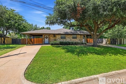 A house with a brown roof and a brown fence is surrounded by green grass and trees.