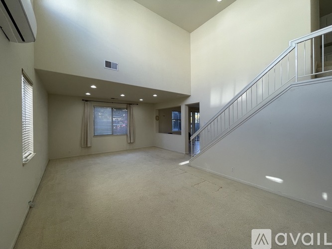 A spacious room with a staircase and a window with curtains.