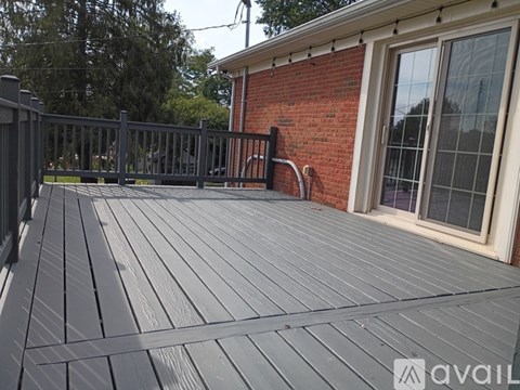 A wooden deck with a black railing and a brick building in the background.