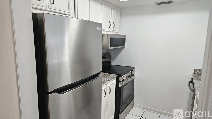 A stainless steel refrigerator stands in a kitchen with white cabinets and a microwave above the oven.