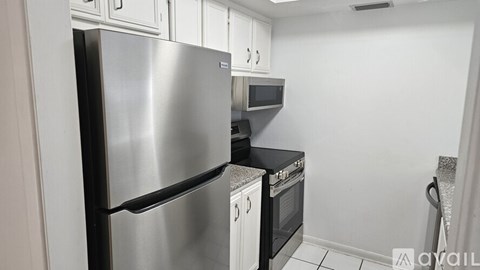 A stainless steel refrigerator stands in a kitchen with white cabinets and a microwave above the oven.