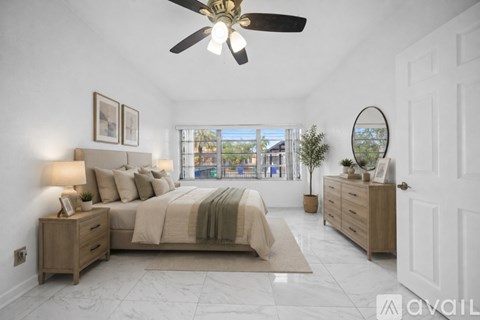 A bedroom with a large bed, a ceiling fan, and a view of the outside through a window.