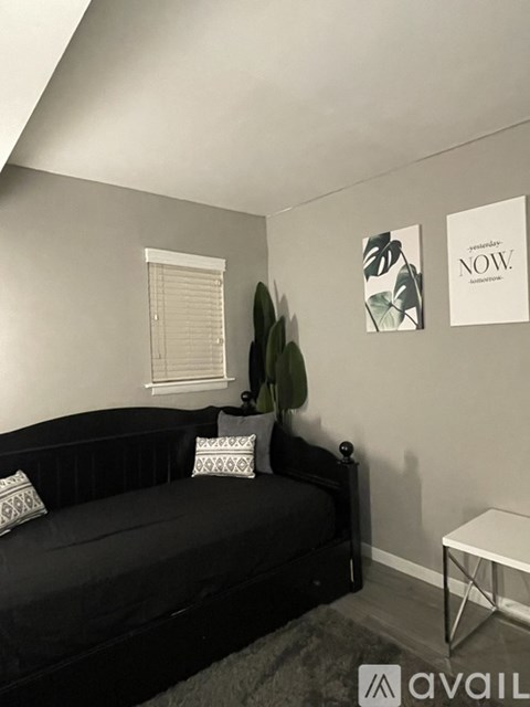 A black couch with a green jacket on it and a white table.