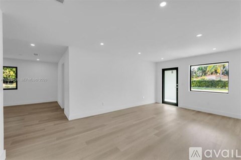 A spacious room with wooden flooring and a large window showing a lush green landscape.