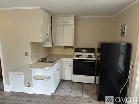 A kitchen with white cabinets and appliances, a black refrigerator, and a tiled floor.