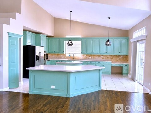 A kitchen with a large island and teal cabinets.