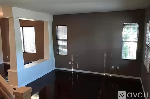 A spacious room with dark flooring and a large window with blinds.