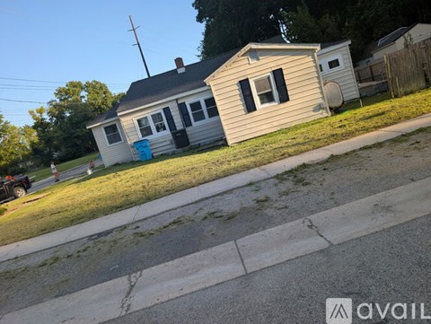 A house with a blue trash can is located on the corner of a street.
