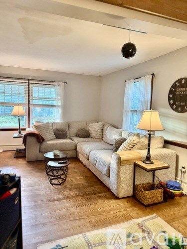 A living room with a couch, a table with a lamp, and a window with curtains.