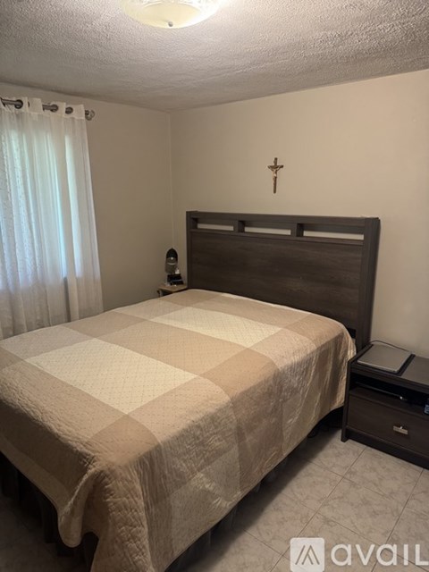 A bedroom with a bed, nightstand, and a cross on the wall.