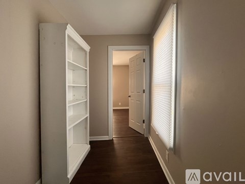 A long hallway with a white door on the right and a white shelving unit on the left.