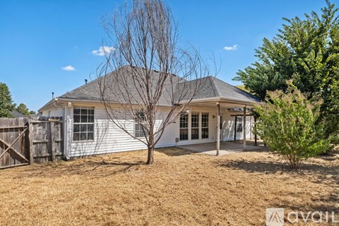 A house with a white exterior and a grey roof is surrounded by a fence and some trees.