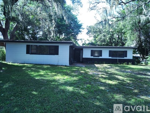 A white house with a black door is surrounded by green grass and trees.