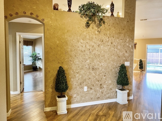 A room with a gold wallpaper and two potted trees.