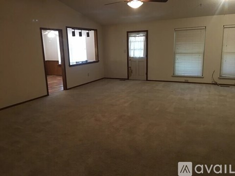 A spacious room with a ceiling fan and three windows.