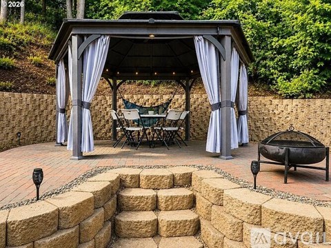 A gazebo with a table and chairs is surrounded by stone steps.