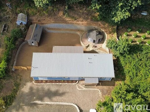An aerial view of a building with a grey roof and a blue roofed structure surrounded by trees.