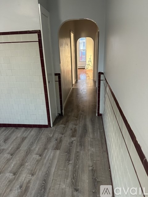 A long hallway with a white tile wall and wood flooring.