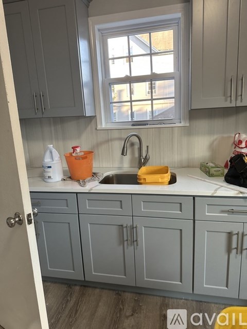 A kitchen with grey cabinets and a window above the sink.