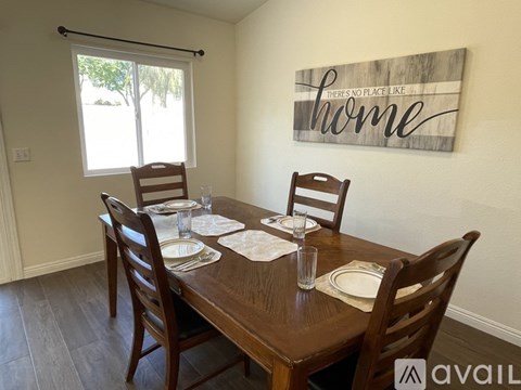 A dining room with a wooden table set for two and a sign that says "There's no place like home.".