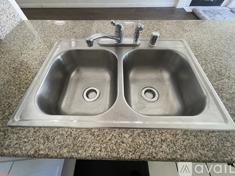 A double sink stainless steel kitchen sink with a granite countertop.